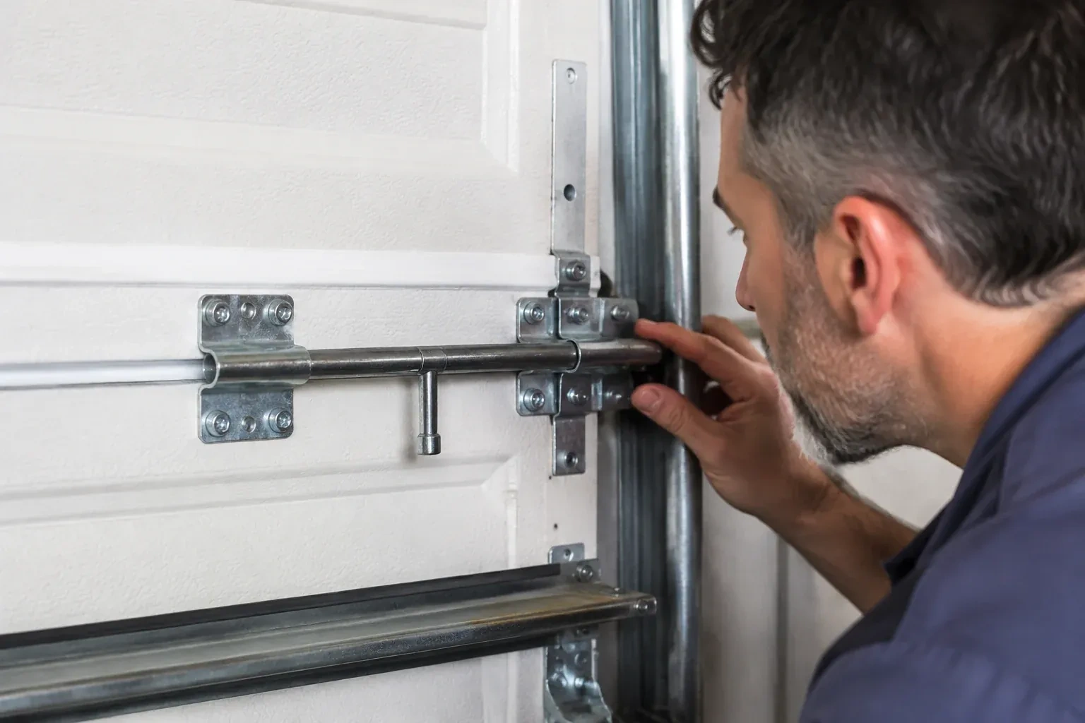 Person leaning close to a white paneled door, one hand on a metal slide-bolt bar mounted across the panel. — Garage Door Manual Lock Repair, Lawrence Manor